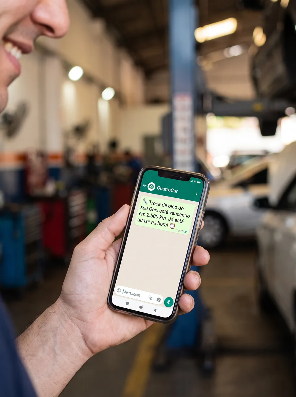 Mão segurando um celular com uma mensagem do QuatroCar no WhatsApp avisando sobre a troca de óleo vencendo